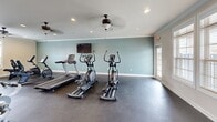 This 650 square foot fitness center, located at 710 Nick Fitcheard Rd NW in Huntsville, AL, offers a well-designed space for exercise enthusiasts. The single-floor layout maximizes functionality, accommodating a wide range of workout equipment. The room features high ceilings with elegant ceiling fans and recessed lighting, creating an airy and inviting atmosphere.

Large windows allow natural light to flood the space, while also offering views of the outdoors. The walls are painted in a combination of neutral tones and a refreshing blue, promoting a calm yet energizing environment. The durable concrete flooring is ideal for heavy equipment and high-traffic areas.

The center is equipped with a diverse selection of fitness machines, including treadmills, ellipticals, stationary bikes, and weight training equipment. Free weights, exercise balls, and other accessories are neatly organized along the walls. The layout provides ample space for both cardio and strength training, ensuring users can move freely between equipment.

Thoughtful additions like a water cooler and strategically placed mirrors enhance the user experience. The facility's design emphasizes cleanliness and order, creating an appealing space that encourages regular exercise and promotes overall well-being.