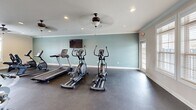 This 650 square foot fitness center, located at 710 Nick Fitcheard Rd NW in Huntsville, AL, offers a well-designed space for exercise enthusiasts. The single-floor layout maximizes functionality, accommodating a wide range of workout equipment. The room features high ceilings with elegant ceiling fans and recessed lighting, creating an airy and inviting atmosphere.

Large windows allow natural light to flood the space, while also offering views of the outdoors. The walls are painted in a combination of neutral tones and a refreshing blue, promoting a calm yet energizing environment. The durable concrete flooring is ideal for heavy equipment and high-traffic areas.

The center is equipped with a diverse selection of fitness machines, including treadmills, ellipticals, stationary bikes, and weight training equipment. Free weights, exercise balls, and other accessories are neatly organized along the walls. The layout provides ample space for both cardio and strength training, ensuring users can move freely between equipment.

Thoughtful additions like a water cooler and strategically placed mirrors enhance the user experience. The facility's design emphasizes cleanliness and order, creating an appealing space that encourages regular exercise and promotes overall well-being.