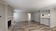 This single-floor residence offers a thoughtfully laid out interior with a blend of modern updates and functional design. The main living area greets you at entry with wood-look plank flooring in a cool gray tone, crown molding, a textured ceiling, and a classic fireplace with a clean white mantle. French doors and multiple windows allow natural light to fill the space, creating an open and airy atmosphere. A pendant light fixture adds a polished touch overhead. Adjacent to the living area, a secondary living or dining space continues the wood-look flooring and features crown molding for a cohesive look. The kitchen is outfitted with white cabinetry, light stone-look countertops, a double stainless steel sink with a brushed nickel faucet, and black appliances. The bedrooms are carpeted for comfort, each featuring neutral walls, textured ceilings, and natural light from windows with blinds. The primary bedroom includes a ceiling fan with light. Two full bathrooms each feature a tub-shower combination with clean white surrounds, hardwood-look flooring, and chrome fixtures. Throughout the residence, consistent neutral tones, white trim, and updated finishes contribute to a cohesive and move-in-ready aesthetic.