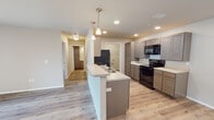 This single-floor residence at 1100 W 14th St in Webb City, Missouri offers a clean, modern aesthetic with an open-concept design that seamlessly connects the living and kitchen areas. Light-toned luxury vinyl plank flooring runs throughout the unit, creating a cohesive and easy-to-maintain foundation that enhances the bright, airy atmosphere.

The kitchen is a standout feature, showcasing taupe-finish shaker-style cabinetry with ample upper and lower storage, including a tall pantry cabinet. Light quartz-style countertops provide generous prep space, while black appliances — including an electric range, over-the-range microwave, and refrigerator — deliver a striking contrast. A peninsula with an integrated sink and pendant lighting overhead makes the kitchen both functional and visually appealing, ideal for casual dining or entertaining.

The living area is generously proportioned, bathed in natural light from a sliding glass door that opens to an outdoor balcony. A ceiling fan with integrated lighting adds comfort and practicality. The bedrooms are well-sized, each featuring ceiling fans and windows with blinds for natural light and privacy. The bathroom is finished with matching cabinetry, a light countertop, and a full tub-shower combination. Recessed lighting throughout the unit adds a polished, contemporary touch to this well-appointed home.