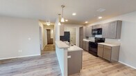 This single-floor residence at 1100 W 14th St in Webb City, Missouri offers a clean, modern aesthetic with an open-concept design that seamlessly connects the living and kitchen areas. Light-toned luxury vinyl plank flooring runs throughout the unit, creating a cohesive and easy-to-maintain foundation that enhances the bright, airy atmosphere.

The kitchen is a standout feature, showcasing taupe-finish shaker-style cabinetry with ample upper and lower storage, including a tall pantry cabinet. Light quartz-style countertops provide generous prep space, while black appliances — including an electric range, over-the-range microwave, and refrigerator — deliver a striking contrast. A peninsula with an integrated sink and pendant lighting overhead makes the kitchen both functional and visually appealing, ideal for casual dining or entertaining.

The living area is generously proportioned, bathed in natural light from a sliding glass door that opens to an outdoor balcony. A ceiling fan with integrated lighting adds comfort and practicality. The bedrooms are well-sized, each featuring ceiling fans and windows with blinds for natural light and privacy. The bathroom is finished with matching cabinetry, a light countertop, and a full tub-shower combination. Recessed lighting throughout the unit adds a polished, contemporary touch to this well-appointed home.