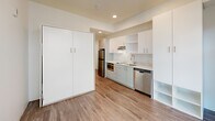 Located at 1075 NW 16th St in Portland's vibrant Northwest District, this efficiently designed studio offers a thoughtfully arranged single-floor layout that maximizes every square foot. The open-plan main area seamlessly integrates the kitchen, dining, and living spaces into one cohesive environment, bathed in natural light from large floor-to-ceiling windows that frame views of the surrounding neighborhood.

The kitchen is outfitted with crisp white upper and lower cabinetry, light-toned countertops, a stainless steel sink, a built-in cooktop, a microwave, a dishwasher, and a full-size stainless steel refrigerator — providing a complete set of modern appliances within a compact footprint. Recessed lighting supplements the natural light throughout.

A built-in wall unit offers generous storage and incorporates open shelving for organizational flexibility. The space also features a Murphy bed integrated into the cabinetry wall, a smart solution that preserves living area during the day. Wood-look plank flooring runs throughout, lending warmth to the otherwise clean, white interior palette.

The bathroom includes a floating white vanity with an undermount sink, a framed mirror, and a separate shower, maintaining the same modern, minimalist aesthetic found throughout the rest of the space.