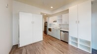 Located at 1075 NW 16th St in Portland's vibrant Northwest District, this efficiently designed studio offers a thoughtfully arranged single-floor layout that maximizes every square foot. The open-plan main area seamlessly integrates the kitchen, dining, and living spaces into one cohesive environment, bathed in natural light from large floor-to-ceiling windows that frame views of the surrounding neighborhood.

The kitchen is outfitted with crisp white upper and lower cabinetry, light-toned countertops, a stainless steel sink, a built-in cooktop, a microwave, a dishwasher, and a full-size stainless steel refrigerator — providing a complete set of modern appliances within a compact footprint. Recessed lighting supplements the natural light throughout.

A built-in wall unit offers generous storage and incorporates open shelving for organizational flexibility. The space also features a Murphy bed integrated into the cabinetry wall, a smart solution that preserves living area during the day. Wood-look plank flooring runs throughout, lending warmth to the otherwise clean, white interior palette.

The bathroom includes a floating white vanity with an undermount sink, a framed mirror, and a separate shower, maintaining the same modern, minimalist aesthetic found throughout the rest of the space.