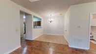 This single-story home offers a well-designed layout with a blend of warm hardwood flooring and plush carpet throughout. The dining area makes a strong first impression with an elegant chandelier overhead and tile flooring that transitions seamlessly into the rich hardwood of the main living spaces. A pass-through opening connects the dining area to the kitchen, which is equipped with warm wood cabinetry, stainless steel appliances including a range and over-the-range microwave, and light granite countertops that extend generously across the workspace. A hallway connects the main living areas to the private quarters of the home, passing by a utility sink area along the way. The primary bedroom is a spacious retreat featuring a tray ceiling with a ceiling fan, hardwood floors, and direct access to an en-suite bathroom. Additional bedrooms are finished with neutral carpet and ceiling fans, with windows that bring in natural light and views of the surrounding greenery. The bathrooms are appointed with granite-topped vanities and a full tub-shower combination with tiled surrounds. Throughout the home, six-panel doors, clean white trim, and a neutral color palette create a cohesive and inviting atmosphere.