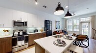 Located at 400 S Hall St in Dallas, Texas, this single-floor residence offers a thoughtfully designed, contemporary living experience. The open-concept kitchen is a standout feature, showcasing a two-tone cabinetry scheme with upper white cabinets and warm wood-finish lower cabinets, complemented by a light green subway tile backsplash and pristine quartz countertops. A large center island with an integrated sink and seating serves as the heart of the space, while stainless steel appliances and bold industrial pendant lighting add a refined, modern edge. Rich wood-look flooring flows throughout, unifying the kitchen with the adjoining living area. The living room is bright and welcoming, bathed in natural light through oversized grid-pane windows and a glass door that opens to an outdoor view, creating an effortless indoor-outdoor connection. The bedroom continues the theme of comfort, featuring large windows with views of the surrounding neighborhood and ample room for a generous furniture arrangement. The bathroom is well-appointed with a wood-toned vanity, quartz countertop, and direct access to a well-organized walk-in closet with built-in shelving. Throughout the residence, clean lines, neutral tones, and carefully considered finishes come together to create a polished, urban living environment.