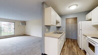 This single-floor unit offers a practical and straightforward layout designed for comfortable everyday living. The kitchen features white cabinetry, a double-door pantry closet with louvered doors, wood-look vinyl flooring, and white appliances including an electric range, microwave, and refrigerator. A countertop sink with ample cabinet storage below completes the galley-style cooking space, which opens toward the main living area.

The living room is generously proportioned, finished with neutral carpet and a ceiling fan, and benefits from a large sliding glass door that invites natural light and provides access to an outdoor balcony with views of the surrounding area. A wall-mounted air conditioning unit and baseboard heating ensure year-round climate control throughout the unit.

The bedrooms are carpeted and well-lit, each featuring windows with outdoor views, baseboard heating, and wall A/C units for individual comfort. Neutral walls and wood-toned baseboards create a clean, understated aesthetic throughout.

The bathroom includes a full tub and shower combination with classic white tile surround, a toilet, and a vanity. Tile flooring adds a practical touch to the space. Overall, the unit presents a functional, no-frills design suited for efficient, comfortable living.