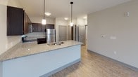 Located at 115 Dayton St in Hamilton, Ohio, this single-floor unit offers a thoughtfully designed layout with contemporary finishes throughout. The kitchen is a standout feature, equipped with rich dark espresso cabinetry, granite-style countertops, and a full suite of stainless steel appliances including a refrigerator, electric range, and over-the-range microwave. A central island with a built-in sink and pendant lighting above provides additional prep space and a natural gathering point that flows seamlessly into the open living area. The living space is bright and airy, with light wood-style flooring, a ceiling fan, and large windows with access to an exterior door, allowing for generous natural light. The bedroom is carpeted for comfort, features a ceiling fan, and includes a large window offering exterior views. Storage is well-addressed with a spacious walk-in closet outfitted with wire shelving and carpeted flooring. The bathroom is accessible via a hallway and includes a toilet and vanity with dark wood cabinetry, consistent with the kitchen's design aesthetic. Light wood-style flooring extends through the hallway and main living areas, tying the space together with a clean, cohesive look.