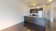 This single-floor residence at Chapel St Novella in New Haven, Connecticut offers a well-designed, contemporary layout that balances functionality with clean, modern aesthetics throughout. The open-concept kitchen serves as a central highlight, featuring dark espresso cabinetry, stainless steel appliances including a refrigerator, range, and built-in microwave, and a granite-topped breakfast bar that extends into the living area. Pendant lighting above the bar adds a polished finishing touch. The living area is finished with dark hardwood-style flooring and large windows fitted with horizontal blinds, allowing ample natural light while maintaining privacy and offering views of the surrounding neighborhood.

The bedrooms are carpeted in a neutral tan tone, providing a comfortable contrast to the harder surfaces elsewhere in the unit. Large windows in the bedrooms bring in generous daylight and frame outdoor views of the neighboring streetscape. At least one bedroom includes access to a walk-in closet. Two bathrooms are present, each featuring dark tile flooring, a soaking tub with shower, white tile surround, and a dark vanity with an integrated sink. The overall palette throughout the unit is neutral and contemporary, with white walls and crisp trim creating a bright, cohesive atmosphere.