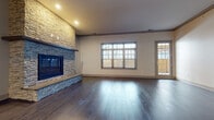 This single-floor residence showcases a thoughtfully designed open layout with consistent, contemporary finishes throughout. The living area serves as a centerpiece, highlighted by a dramatic floor-to-ceiling stacked stone fireplace and dark hardwood flooring that extends through the main living spaces. Large windows and a glass door flood the room with natural light and provide views of the outdoors.

The kitchen is well-appointed with gray shaker-style cabinetry, glass-front upper cabinets, a geometric patterned tile backsplash, and light stone countertops. A contrasting blue island anchors the space, while stainless steel appliances, including a gas range with hood, refrigerator, and dishwasher, complete the functional design. Pendant lighting adds a refined touch above the island.

Bedrooms feature plush carpeting, neutral walls, and windows with blinds. The primary bathroom offers a double-sink vanity with stone countertops, framed mirror, and large-format tile flooring. A spacious walk-in closet with built-in shelving and hanging rods provides ample storage. The dedicated laundry room includes a stacked washer and dryer set atop tile flooring, rounding out this well-organized home.