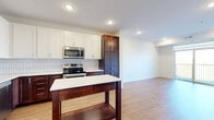 Located at 251 Eldorado Dr in Jordan, MN, this thoughtfully designed 2-bedroom, 2-bathroom residence offers a clean, modern aesthetic across a single floor. The open-concept kitchen and living area serves as the heart of the home, featuring a striking two-tone cabinetry scheme with rich dark wood lower cabinets paired with crisp white uppers, a herringbone tile backsplash, stainless steel appliances, and a central kitchen island with a white countertop. Light wood-style flooring runs throughout the entire residence, creating a warm and cohesive feel. The spacious living area flows naturally from the kitchen and opens to a private balcony through sliding glass doors, bringing in abundant natural light and outdoor views of the surrounding landscape. Both bedrooms are generously sized, bright, and feature windows that invite natural light. The primary bedroom is particularly spacious and benefits from its own closet. The two bathrooms are well-appointed with dark wood vanities, white countertops, and wood-look flooring. One bathroom conveniently houses a stacked washer and dryer. Three closets provide ample storage, and a dedicated utility room adds further practicality. Recessed lighting throughout enhances the clean, modern ambiance of this well-appointed residence.