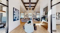 Located at Hammond Center Drive in Raleigh, NC, this impressive single-floor amenity center offers a wealth of well-appointed spaces designed for comfort, productivity, and wellness. The main living area is a true showpiece, featuring soaring ceilings with striking dark wood coffered beams, light hardwood flooring, and an eye-catching cluster chandelier. Curated contemporary artwork adorns the walls, while multiple seating arrangements, a billiards table, and built-in media wall with booth-style seating create a dynamic social environment. A wet bar area with warm wood cabinetry adds convenience. The second living area transitions to a softer aesthetic, with patterned carpet, a built-in banquette upholstered in bold blue, and an adjacent reception workspace featuring dark cabinetry and textile wall art beneath a dramatic double-height ceiling. The dedicated office space is bright and professional, surrounded by large windows with roller shades and outfitted with a conference table and leather chairs beneath a statement drum pendant light. The exercise room is comprehensively equipped with cardio machines, strength equipment, ceiling fans, and ample natural light, complemented by a mirrored studio space with a sage green shiplap accent wall for cycling and additional workouts.