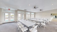 This single-floor facility is thoughtfully designed to accommodate a variety of gatherings and activities. The main event room is bright and airy, featuring large floor-to-ceiling windows and glass-paneled French doors that allow abundant natural light to fill the space while offering views of the surrounding area. Neutral-toned walls, recessed lighting, and dual ceiling fans create a comfortable and welcoming atmosphere. The room is furnished with rows of white folding tables and chairs, making it well-suited for meetings, classes, workshops, or social events.

Adjacent to the event room is an open multipurpose studio with light wood-look flooring, full-wall mirrors, recessed lighting, and ceiling fans. This flexible space is ideal for fitness classes, dance, yoga, or other active uses. Natural light streams in through multiple windows, and the mirrored wall enhances the sense of openness.

A connecting corridor links the two primary spaces and features a wall-mounted flat-screen display, providing a practical communication or presentation hub. The transition between areas is marked by elegant white French doors with glass insets set against exposed brick accents, adding a refined architectural touch. Throughout the facility, clean finishes, neutral palettes, and smart climate controls contribute to a polished, functional, and inviting environment.