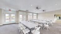 This single-floor facility is thoughtfully designed to accommodate a variety of gatherings and activities. The main event room is bright and airy, featuring large floor-to-ceiling windows and glass-paneled French doors that allow abundant natural light to fill the space while offering views of the surrounding area. Neutral-toned walls, recessed lighting, and dual ceiling fans create a comfortable and welcoming atmosphere. The room is furnished with rows of white folding tables and chairs, making it well-suited for meetings, classes, workshops, or social events.

Adjacent to the event room is an open multipurpose studio with light wood-look flooring, full-wall mirrors, recessed lighting, and ceiling fans. This flexible space is ideal for fitness classes, dance, yoga, or other active uses. Natural light streams in through multiple windows, and the mirrored wall enhances the sense of openness.

A connecting corridor links the two primary spaces and features a wall-mounted flat-screen display, providing a practical communication or presentation hub. The transition between areas is marked by elegant white French doors with glass insets set against exposed brick accents, adding a refined architectural touch. Throughout the facility, clean finishes, neutral palettes, and smart climate controls contribute to a polished, functional, and inviting environment.