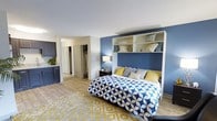 Located at 9015 10 Mile Road in Knoxville, Tennessee, this single-floor studio unit offers a smartly designed open-concept layout that maximizes both functionality and style. The main living area serves as the centerpiece of the space, anchored by a built-in Murphy bed framed with integrated shelving above — a standout feature that blends storage and sleeping quarters seamlessly. A bold navy blue accent wall adds depth and character, complemented by light wood-style flooring that runs throughout, brightening the interior and creating a sense of warmth. The open layout allows the sleeping, living, and kitchen areas to flow naturally into one another. The kitchen features navy cabinetry with light countertops, offering a cohesive color palette that ties the space together. A generously sized walk-in closet provides ample storage, visible just off the main living area. The unit's neutral white ceilings and walls provide a clean backdrop that enhances the overall brightness of the interior. The thoughtful use of color, built-in storage solutions, and durable finishes make this a practical yet visually appealing space well-suited for comfortable everyday living in the Knoxville area.