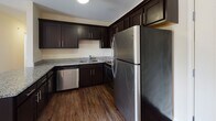 Located at 9512 Transit Rd in East Amherst, NY, this single-floor unit offers a well-designed layout with a cohesive blend of modern finishes and functional living spaces. The open living area is a standout feature, showcasing rich hardwood-style flooring, neutral walls, and a fireplace that serves as a natural focal point. A large sliding glass door floods the space with natural light while providing views of the surrounding greenery, creating an inviting and airy ambiance.

The kitchen is thoughtfully appointed with dark espresso cabinetry, granite countertops, stainless steel appliances including a refrigerator, dishwasher, and range, and durable hardwood-style flooring that continues from the main living area. A pendant light fixture accents the dining transition space near the entry.

The bedroom features plush wall-to-wall carpeting, a ceiling fan with light, and a window fitted with blinds that allows for natural light while maintaining privacy.

The bathroom is well-equipped with accessibility in mind, featuring stainless steel grab bars near the tub-shower combination, a dark-cabineted vanity with granite countertops, a large mirror, and tile flooring throughout. The overall design is clean, modern, and move-in ready.
