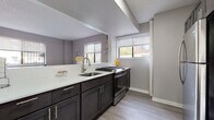 This single-floor residence offers a thoughtfully designed layout that balances modern aesthetics with everyday functionality. The kitchen is a standout feature, showcasing dark espresso shaker-style cabinetry paired with crisp white quartz countertops and a classic subway tile backsplash. A stainless steel gas range and an undermount sink with a brushed nickel faucet complete the space, while multiple windows flood the area with natural light and provide views of the surrounding neighborhood. Light wood-tone flooring runs throughout, lending warmth and continuity to the home. The living area is spacious and inviting, centered around large windows that bring in ample daylight. Light gray walls and wood-tone floors create a neutral, versatile backdrop. The bedroom is a serene retreat, finished in soft taupe tones with multiple windows offering natural light and outdoor views. The light hardwood flooring continues here, complementing the calm and restful atmosphere. The bathroom is finished with floor-to-ceiling marble-look tile, a deep soaking tub with overhead shower, a white pedestal-style vanity, and gray floor tiles — creating a clean, spa-inspired feel. Overall, the space presents a cohesive, modern design with neutral tones, quality finishes, and an abundance of natural light throughout.