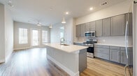 Located in Austin, TX (78717), this well-designed 2-bedroom, 2-bathroom residence offers a thoughtful single-floor layout with modern finishes throughout. The open-concept kitchen and living area serves as the heart of the home, featuring gray shaker-style cabinetry, a white quartz waterfall island with an undermount sink and gold-toned faucet, subway tile backsplash, and stainless steel appliances including a gas range and microwave. Pendant lighting and recessed fixtures illuminate the space, while light hardwood-style flooring and a ceiling fan with outdoor access create a bright, airy atmosphere. The living area benefits from natural light streaming through large windows and a glass-paneled door. Both bedrooms are carpeted and offer a calm, neutral palette with ample natural light; the primary bedroom is generously sized and includes a dedicated walk-in closet. Each bathroom is finished with large-format tile flooring and gray vanity cabinetry. The primary bath features a marble-surround soaking tub and a separate glass-enclosed walk-in shower, while the second bath includes a glass-enclosed shower and overhead cabinetry. Both bathrooms provide direct access to walk-in closets, maximizing storage and functionality throughout the home.