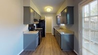 This 2-bedroom, 2-bathroom residence is a well-organized single-story unit designed for comfortable everyday living. The galley-style kitchen features gray cabinetry on both sides, light-toned countertops, black appliances including a range and refrigerator, and wood-look flooring that extends through the main living areas. Adjacent to the kitchen, the dining area benefits from natural light via a large window and connects seamlessly to the living room. The living room is a standout space, highlighted by a classic wood-burning fireplace with a white mantel, wood-look flooring, a ceiling fan with light fixture, and a window that brings in natural light. Both bedrooms are carpeted and feature ceiling fans, neutral gray walls, and windows with blinds that allow for ample natural light. The primary bedroom includes direct access to one of the two bathrooms, each of which is equipped with a tub-shower combination, tile flooring, and clean, neutral finishes. The layout, as seen in the overhead model view, demonstrates an efficient use of space with a clear separation between living and sleeping areas, making this a practical and comfortable home.
