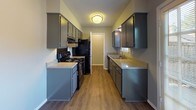 This 2-bedroom, 2-bathroom residence is a well-organized single-story unit designed for comfortable everyday living. The galley-style kitchen features gray cabinetry on both sides, light-toned countertops, black appliances including a range and refrigerator, and wood-look flooring that extends through the main living areas. Adjacent to the kitchen, the dining area benefits from natural light via a large window and connects seamlessly to the living room. The living room is a standout space, highlighted by a classic wood-burning fireplace with a white mantel, wood-look flooring, a ceiling fan with light fixture, and a window that brings in natural light. Both bedrooms are carpeted and feature ceiling fans, neutral gray walls, and windows with blinds that allow for ample natural light. The primary bedroom includes direct access to one of the two bathrooms, each of which is equipped with a tub-shower combination, tile flooring, and clean, neutral finishes. The layout, as seen in the overhead model view, demonstrates an efficient use of space with a clear separation between living and sleeping areas, making this a practical and comfortable home.