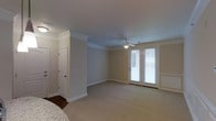 This two-story home combines traditional design elements with comfortable, functional living spaces throughout. The interior is characterized by neutral, warm-toned walls that create a welcoming and versatile backdrop for any décor style. Crown molding runs along the ceilings, adding a refined architectural detail that elevates the overall aesthetic of the space. The flooring transitions thoughtfully between plush carpeting in the main living areas and hardwood in connecting hallways or entryways, offering both comfort and durability. A ceiling fan with a built-in light fixture serves as a practical focal point in the main living area, promoting air circulation and illumination. French doors with slatted blinds provide access to an outdoor area while allowing natural light to filter into the room, contributing to a bright and airy ambiance. White panel doors and crisp white baseboards contrast cleanly against the neutral walls, reinforcing the home's classic, cohesive design language. The layout across two floors allows for a clear separation between living and private spaces, making the home well-suited for both everyday living and entertaining.