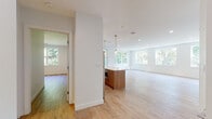Located at 50 Peter Kristof Way in Medfield, Massachusetts, this contemporary single-floor residence offers a thoughtfully designed open-concept layout with high-end finishes throughout. Light hardwood flooring flows seamlessly across the main living areas, complementing the bright, neutral palette of the crisp white walls and ceilings fitted with recessed lighting.

The kitchen is a standout centerpiece, featuring a large island with a quartz countertop, warm wood cabinetry paired with white upper cabinets, gold hardware accents, a light blue subway tile backsplash, and stainless steel appliances including a gas range and refrigerator. Stylish pendant lights hang above the island, adding a refined touch. The kitchen opens directly to a spacious living area bathed in natural light from large multi-pane windows that frame picturesque views of surrounding greenery.

The primary bathroom is finished with large-format tile flooring, a wall-mounted toilet, a glass-enclosed shower with marble-style tile, and a wood-toned vanity. A generously sized walk-in closet with wire shelving provides ample storage. The overall ambiance of the space is clean, modern, and airy, making it a bright and inviting place to call home.
