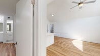 This single-floor unit presents a clean, modern aesthetic defined by crisp white walls, light-toned hardwood flooring, and an open layout that encourages natural light throughout. The living area benefits from dramatic vaulted ceilings, lending a sense of openness and volume that extends into the adjoining kitchen. A ceiling fan overhead adds a practical touch to the airy space.

The kitchen is thoughtfully designed with white shaker-style cabinetry, a subway tile backsplash, white quartz countertops, and a full suite of stainless steel appliances, including a refrigerator, electric range, and built-in microwave. A peninsula with an integrated sink connects the kitchen to the living area, creating a seamless flow ideal for entertaining or everyday use. A louvered closet door near the kitchen provides additional storage.

The bedrooms are well-proportioned, each featuring light wood flooring, white walls, and windows fitted with blinds that frame views of surrounding greenery. One bedroom includes a dedicated closet and direct access to a bathroom with white cabinetry and a vanity mirror. Throughout the unit, consistent finishes and a neutral palette create a cohesive, move-in-ready environment.
