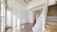 Located at 123 Aldrin Dr NW in Huntsville, Alabama, this two-story space is thoughtfully designed with a clean, modern aesthetic throughout. The main floor is the larger of the two levels and makes an immediate impression with its dramatic vaulted ceilings in the living room, where a large multi-pane window arrangement floods the space with natural light and offers views of the surrounding neighborhood. A ceiling fan with a stylish brushed brass fixture complements the soaring height, while light-toned hardwood flooring flows seamlessly throughout.

The kitchen is well-appointed with gray shaker-style cabinetry, white herringbone tile backsplash, light countertops, and a full suite of stainless steel appliances including a refrigerator, electric range, built-in microwave, and dishwasher. A wine rack cabinet adds a distinctive touch. The bathroom features matching gray cabinetry, a framed vanity mirror, white countertop, and hardwood-style flooring, maintaining a consistent design language.

The upper level, accessed via staircase, offers a versatile open area bathed in natural light from multiple windows, accented by vaulted ceilings and a clean white palette. The space is finished with the same light hardwood flooring, giving the entire home a cohesive and contemporary feel throughout.