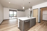 This contemporary 1-bedroom, 1-bathroom unit offers a well-designed open-concept layout that efficiently combines the kitchen and living area into a single, cohesive space. Light hardwood flooring runs throughout, creating a warm and consistent aesthetic across every room. The kitchen is a functional centerpiece, anchored by a large island with a white quartz countertop, an integrated sink, and a dishwasher. Wood-toned cabinetry complements a full suite of stainless steel appliances, including a refrigerator, electric range, and over-the-range microwave. Pendant lighting above the island adds a modern, finished touch. Exposed cylindrical ductwork runs through the living area and bedroom, lending an urban, industrial character to the space. Large black-framed windows in both the living area and bedroom invite abundant natural light and frame elevated views of the surrounding cityscape. The bedroom is a well-proportioned private retreat with its own window and access to a dedicated closet. The bathroom features wood-toned cabinetry with a white countertop vanity, hardwood flooring, and clean white walls, maintaining the unit's modern design language throughout.