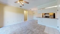 Located at 10011 Balaye Run Dr in Tampa, FL, this single-floor residence offers a thoughtfully designed layout that maximizes comfort and functionality. The open-concept living and dining area is finished with plush carpeting, crown molding, and a ceiling fan, while a chandelier adds an elegant touch overhead. A sliding glass door floods the space with natural light and opens onto a private balcony overlooking lush, mature trees. The galley-style kitchen is equipped with light wood cabinetry, granite-style countertops, black appliances including a refrigerator and range, and tile flooring. A peninsula with a built-in sink and breakfast bar connects the kitchen seamlessly to the living area. The spacious bedroom features carpeting, crown molding, a ceiling fan, and direct access to a generously sized walk-in closet outfitted with wire shelving on multiple walls. The full bathroom includes a granite-topped vanity with white cabinetry, a tiled tub-shower combination, and tile flooring. Additional conveniences include an in-unit laundry area and a hallway providing practical access throughout the home. The warm, neutral color palette creates a bright and welcoming ambiance throughout the entire space.