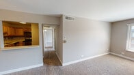 Located at 970 Jefferson Square in Elk Grove Village, Illinois, this single-floor residence offers a practical and comfortable layout designed for everyday living. The living area is generously sized, finished with plush carpeting and neutral taupe walls that create a warm, inviting atmosphere. A ceiling fan with an integrated light fixture anchors the space, while a pass-through window connects the living area directly to the kitchen, enhancing the open feel between the two spaces.

The kitchen is well-appointed with warm oak cabinetry, light countertops, and a striking mosaic tile backsplash. Stainless steel appliances — including a range, microwave, and dishwasher — provide a modern, functional cooking environment.

A carpeted hallway leads to the bedrooms, each finished with neutral tones and plentiful natural light from large windows with blinds. One bedroom features an expansive wall of built-in closets, offering exceptional storage capacity. The bathroom includes a single-sink vanity with a white cabinet, a toilet, and a walk-in shower enclosed by sliding frosted glass doors, all set on clean tile flooring.

Throughout the residence, consistent neutral color palettes, white trim, and carpet flooring contribute to a cohesive, move-in-ready aesthetic.