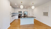 This well-appointed 2-bedroom, 2-bathroom residence in Mooresville, NC offers a thoughtfully designed open-concept layout filled with clean lines and modern finishes. The combined kitchen and living area serves as the heart of the home, where light hardwood flooring flows seamlessly throughout. The kitchen is a standout, featuring white shaker cabinetry with matte black hardware, dark quartz countertops, a subway tile backsplash, stainless steel appliances, and a large center island illuminated by two globe pendant lights with brushed gold accents. The spacious living room opens to a private balcony through French doors, with additional windows inviting generous natural light and a ceiling fan overhead. Both bedrooms are carpeted and bright, each equipped with a ceiling fan and windows overlooking the surroundings. The primary bedroom is generously sized and connects to a well-designed en-suite bathroom featuring a wide double-sink vanity with dark quartz countertops, white cabinetry, matte black fixtures, and a large mirror with modern lighting. A spacious walk-in closet with wire shelving provides abundant storage. The second bathroom maintains the same cohesive, contemporary aesthetic found throughout the home.