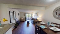 This single-floor residence offers a thoughtfully organized layout that maximizes comfort and functionality throughout. The open-concept living area is anchored by rich hardwood flooring that extends seamlessly through the main spaces, creating a warm and cohesive atmosphere. A large sliding glass door floods the living room with natural light and provides direct access to a private balcony, where views of surrounding greenery can be enjoyed. The living room comfortably accommodates a full seating arrangement and entertainment setup, making it an inviting space for relaxing or hosting.

Adjacent to the living area, a dedicated dining space features room for a full dining table and chairs, accented by a decorative mirror that adds depth to the area. A sliding closet adds practical storage nearby.

The galley-style kitchen is equipped with rich wood cabinetry, a double-basin sink, granite-style countertops, and white appliances including a range and dishwasher. A breakfast bar counter provides additional prep space and casual seating potential.

The bedroom is a serene retreat with a large window fitted with vertical blinds that allow for natural light control, complemented by carpet flooring and ample space for full bedroom furnishings.

The bathroom features a combined tub and shower with clean tile surround, a toilet, and a ventilation unit, completing this functional and comfortable residence.