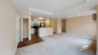 This single-floor unit is located along East Mission Avenue in Spokane, Washington, and features a practical, open-concept layout with warm neutral tones throughout. The living area is finished with plush light-colored carpeting and recessed lighting set into a subtly tiered ceiling, creating a clean and comfortable atmosphere. A six-panel entry door opens into the space, where hardwood-style flooring transitions into the kitchen and entryway zones.

The kitchen is well-appointed with white shaker-style cabinetry, dark laminate countertops, and stainless steel appliances including a refrigerator and range. A peninsula with a built-in sink and additional counter space extends into the open area, providing a natural division between the kitchen and living space while maintaining an open feel. Overhead lighting illuminates the kitchen effectively.

The bedroom features soft carpeting, warm beige walls, a baseboard heater, and a window that admits natural light and views of surrounding greenery, creating a calm retreat. A closet with a rod and shelf provides practical storage.

The bathroom includes a full tub and shower combination with chrome fixtures and a clean white surround. Throughout the unit, consistent neutral wall tones and functional finishes create a cohesive, move-in ready environment.