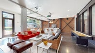 Located at 41 E. 9th Ave. in Columbus, Ohio, this single-floor industrial-chic space blends raw architectural character with modern design to create a versatile and inviting environment. Exposed brick walls serve as a defining feature throughout, complemented by dramatic steel cross-bracing elements that reinforce the space's industrial aesthetic. Polished concrete floors extend across the entire floor plan, adding a sleek, contemporary contrast to the warm, textured brickwork.

One of the most striking architectural features is the full-width glass garage door that opens the space directly to an outdoor patio, flooding the interior with natural light and seamlessly connecting indoor and outdoor areas. A set of globe pendant lights hangs above the kitchen zone, which includes a large white island, built-in sink, countertop appliances, and ample prep space — ideal for catering or communal gatherings.

The lounge area is generously proportioned, furnished with mid-century modern seating, low-profile coffee tables, and eclectic accent pieces that contribute to a curated yet relaxed atmosphere. A bar-height counter with stools provides additional seating near the kitchen. The entry corridor features exposed brick, polished concrete, and a warm wood reception console, setting a welcoming tone upon arrival. Large glass interior partitions and doors enhance visual connectivity throughout the space.