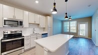 This thoughtfully laid-out one-bedroom, one-bathroom unit offers a functional and modern living environment across a single floor. The kitchen serves as a central highlight, featuring crisp white cabinetry, a classic white subway tile backsplash, quartz countertops, and a full suite of stainless steel appliances including a refrigerator, range, microwave, and dishwasher. A central island with pendant lighting above provides additional prep space and visual separation from the living area.

The living room is bright and inviting, finished with wood-look flooring, neutral-toned walls, and a ceiling fan. Large windows fitted with horizontal blinds allow ample natural light, while a glass-paned door provides direct access to an outdoor balcony area with exterior views.

The bedroom is carpeted for comfort and includes a dedicated closet with wire shelving. A ceiling fan and a window overlooking the outdoors complete the room. The full bathroom is elongated and well-appointed, featuring a single-sink vanity with white cabinetry, a large mirror, wood-look flooring, and a tiled walk-in shower with glass enclosure. A dedicated in-unit laundry area accommodates a full-size washer and dryer with overhead shelving for storage.