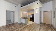 Located at 2010 Euclid Ave in Cleveland's dynamic midtown corridor, this two-bedroom, two-bathroom unit blends industrial character with functional residential design. The single-floor layout makes efficient use of its well-proportioned footprint, offering a cohesive flow between living areas.

The combined kitchen and living area anchors the unit, featuring durable hardwood-style plank flooring and a peninsula kitchen with dark laminate countertops, light maple cabinetry, built-in cooktop, microwave, and full-size refrigerator. Exposed ductwork runs along the ceiling, reinforcing the building's urban, loft-inspired aesthetic. Whitewashed brick accent walls and large windows throughout allow natural light to filter into the space.

Both bedrooms are carpeted for comfort, with the spacious primary bedroom offering an en-suite bathroom accessible through a sliding door. The primary bath includes a wood-toned vanity, large mirror, tile flooring, and a tub-shower combination. The second bedroom is generously sized with its own nearby full bathroom of similar finish and design. A dedicated closet provides additional storage. The overall ambiance is modern industrial, well-suited for urban living in the heart of Cleveland.