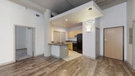 Located on Euclid Avenue in the heart of Cleveland, OH, this two-bedroom, two-bathroom residence blends industrial character with modern comfort across a single floor. The open-concept kitchen and living area serves as the central hub of the home, featuring wood-look plank flooring, a peninsula with a built-in cooktop and dark countertop, light maple cabinetry, black appliances including a refrigerator and dishwasher, and recessed lighting beneath a defined ceiling drop. Exposed ductwork and structural columns add an authentic loft aesthetic throughout. The living area flows toward a balcony, bringing in natural light through large windows set against painted brick walls. The primary bedroom is generously sized, carpeted for comfort, and features tall ceilings, exposed ductwork, and a sliding door that connects directly to an en-suite bathroom equipped with a wood-toned vanity, tiled flooring, and a full tub-shower combination. The second bedroom, also carpeted with a window view, offers a calm and functional space. A second full bathroom mirrors the same clean, tile-and-wood vanity design. Additional highlights include seven closets for abundant storage, an in-unit laundry area, and a private balcony — completing this well-appointed urban retreat.