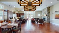 Located at 2020 Proximity Dr in Charleston, SC, this single-floor clubhouse at Westerly Apartment Homes is a beautifully appointed community gathering space that seamlessly blends rustic charm with modern functionality. The interior is defined by its dramatic vaulted ceilings adorned with an intricate system of exposed wood beam trusses, supported by natural wood columns that anchor the open floor plan with architectural distinction.

Rich, warm hardwood flooring flows throughout the main areas, enhancing the inviting ambiance. The great room features a full-height stacked stone fireplace as a commanding focal point, surrounded by comfortable seating areas ideal for relaxation or socializing. Large windows allow abundant natural light to fill the space and offer views of the surrounding landscape.

The fully equipped kitchen is outfitted with dark wood cabinetry, granite countertops, a farmhouse sink, stainless steel appliances, and a central island — designed to support community events and gatherings. An adjacent dining area accommodates multiple seating arrangements for large groups.

A private leasing office area, enclosed with glass partitions and sliding doors, provides a professional workspace within the same footprint. Accent artwork and thoughtful décor details throughout contribute to a welcoming, upscale atmosphere suited for both community engagement and day-to-day operations.