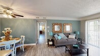 Located at 3851 Cape Landing Dr in Myrtle Beach, SC, this single-floor home offers a thoughtfully designed layout with a cohesive coastal-inspired color palette throughout. The living area is a comfortable, open space featuring wood-look flooring, soothing sage-green accent walls, and a textured ceiling. A large sliding glass door floods the room with natural light and provides access to the outdoors. The adjacent dining area is defined by a striking teal accent wall and ceiling fan, creating an inviting setting for meals. The galley-style kitchen is well-appointed with white cabinetry, light countertops, a double stainless steel sink, and white appliances, all complemented by wood-look flooring. Both bedrooms are carpeted and feature neutral tones, natural light from windows with blinds, and tasteful wall accents that add character to each room. The full bathroom offers a clean, functional design with a white vanity, tub-shower combination, and wood-look flooring. A dedicated laundry room provides added convenience, complete with washer hookups and extra space for organization. Throughout the home, consistent flooring, neutral tones, and coastal accents create a harmonious and welcoming atmosphere.