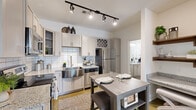 Located at 1000 Sweet Almond Dr in Holly Springs, NC, this single-story residence offers a thoughtfully designed layout across one floor. The open-concept kitchen is a standout feature, equipped with stainless steel appliances including a range, microwave, dishwasher, and refrigerator, complemented by sleek granite countertops, a stainless steel farmhouse sink, and soft gray shaker-style cabinetry with a classic white subway tile backsplash. Track lighting overhead and a built-in wine rack add both function and character. A dining area adjacent to the kitchen provides a casual space for meals.

The living room is bright and welcoming, benefiting from natural light streaming through double French doors topped with a transom window that offer outdoor views. The bedroom is a comfortable retreat with large windows, a ceiling fan, and direct access to a dedicated walk-in closet with built-in shelving. The bathroom features a walk-in shower with a tile surround and granite vanity countertop, maintaining the consistent, refined aesthetic found throughout the home. Warm-toned flooring ties each space together, creating a cohesive and inviting atmosphere throughout this efficiently designed residence.