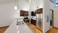 This one-bedroom apartment at 1101 Hawthorne Lane blends industrial character with modern finishes. Soaring ceilings and original hardwood floors define the open living area, while exposed brick columns and raw concrete accents speak to the building's historic conversion. The kitchen is well-appointed with dark wood cabinetry, stainless steel appliances, granite countertops, and pendant lighting overhead. The spacious bedroom benefits from large windows that invite natural light and offer street views. Natural materials, high ceilings, and a loft-like aesthetic create a distinctive urban ambiance throughout this efficiently designed Charlotte residence.