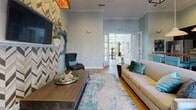 Located at 6880 Rivers Ave in North Charleston, SC, this single-story community clubhouse offers a cohesive blend of modern design and coastal-inspired aesthetics. The bright, airy entrance lobby features large-format light tile flooring, soaring ceilings, and French doors that invite natural light to flood the space. It opens seamlessly into an office area adorned with grasscloth-textured walls, abstract artwork, and warm pendant lighting, creating a welcoming and professional atmosphere.

The lounge area serves as a central gathering space, showcasing hardwood floors, crown molding, and a dramatic floor-to-ceiling chevron-patterned tile fireplace surround. Curated abstract artwork in teal and gold tones complements plush seating and a statement pendant light fixture overhead.

The kitchen is fully equipped with dark espresso cabinetry, a mosaic tile backsplash, stainless steel appliances, and a rustic wood-top island with vibrant teal bar seating beneath large industrial pendant lights. French doors provide direct access to the outdoors.

The fitness center is generously sized and well-lit by rows of windows with plantation shutters. It features a ceiling fan, large wall mirrors, a wall-mounted television, and a comprehensive selection of equipment including ellipticals, cable machines, free weights, and stability accessories — catering to a full range of workout routines.