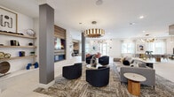 Located in Oviedo, Florida, this sophisticated single-story clubhouse space offers a generously proportioned, open-plan layout designed for both socializing and relaxation. The interior is anchored by a dramatic living lounge area featuring plush seating — including velvet barrel chairs with gold-toned bases — arranged around a textured area rug beneath a striking cylindrical gold pendant chandelier. A built-in fireplace framed by a richly textured accent wall serves as a bold focal point, flanked by open display shelving adorned with curated décor.

Large windows dressed in sheer curtains flood the space with natural light, enhancing the bright, airy atmosphere created by the white tile flooring with inlaid linear detailing. A communal dining zone accommodates a large wooden table and seating, positioned beneath an avant-garde sculptural gold chandelier. Adjacent to it, a full kitchen bar with cabinetry, stainless steel appliances, a mounted display screen, and pendant lighting offers a functional yet stylish gathering hub.

A casual café-style lounge area features built-in banquette seating against a warm wood-panel accent wall, paired with bistro tables and modern chairs. Intimate private booth nooks provide semi-enclosed seating, ideal for quiet conversations. Throughout, curated artwork and layered lighting create a cohesive, upscale ambiance.