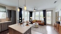 This thoughtfully designed 2-bedroom, 2-bathroom residence offers a single-floor open-concept layout that maximizes comfort and functionality. The living area is a standout feature, bathed in abundant natural light through a sweeping bank of large windows framed by dramatic floor-length black drapes. A ceiling fan overhead and warm hardwood-style flooring underfoot contribute to the inviting ambiance, while direct access to an outdoor balcony extends the living space further.

The kitchen is outfitted with contemporary dark wood-grain cabinetry, crisp white countertops, and a full suite of stainless steel appliances including a refrigerator, range, microwave, and dishwasher. A peninsula provides additional counter space and casual seating, connecting the kitchen seamlessly to the living and dining areas.

Each bedroom is generously sized with plush carpeting, ceiling fans, and ample natural light. Both rooms are complemented by dedicated walk-in or reach-in closets offering strong storage capacity. The two bathrooms are finished with wood-toned vanities, white countertops, and light hardwood-style flooring. One bathroom features a soaking tub with subway tile surround, while the other offers a glass-enclosed walk-in shower, providing distinct and functional options for residents.