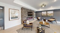 Located at 501 Gateway Blvd in Burnsville, Minnesota, this single-floor community amenity space is thoughtfully designed to blend modern aesthetics with comfortable functionality. The layout flows seamlessly between a fully equipped kitchen and multiple distinct lounge areas, all unified by light hardwood-style flooring throughout.

The kitchen is a standout feature, boasting dark wood cabinetry, a striking marble-look tile backsplash, stainless steel appliances, and an extended island with quartz countertops and leather bar seating. A distinctive slatted wood ceiling adds warmth and architectural texture overhead, complemented by modern pendant lighting.

Adjacent to the kitchen, the main lounge area offers generous open space with a curated mix of contemporary furnishings, including plush sofas, accent chairs, and natural wood coffee tables. Deep slate-blue accent walls provide a sophisticated backdrop for landscape artwork. A separate seating alcove anchors around a floor-to-ceiling stacked stone fireplace wall, complete with a mounted flat-screen TV, built-in shelving, and a dramatic pendant light fixture.

Large windows flood the space with natural light and frame views of the surrounding Burnsville landscape. The overall ambiance is warm, modern, and inviting, making it an ideal gathering and relaxation space.