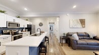 Located on Grand Ave in Palm Coast, Florida, this thoughtfully designed single-story home offers four bedrooms and three bathrooms within a well-utilized floor plan. The open-concept kitchen and living area serves as the heart of the home, featuring white shaker cabinetry, a bold navy herringbone tile backsplash, stainless steel appliances, and a striking blue-accented island with a built-in sink and bar seating — ideal for casual dining and entertaining. The living room flows seamlessly from the kitchen, highlighted by crown molding, recessed lighting, and warm hardwood-style flooring that runs throughout the home. Natural light enters through multiple windows, lending a bright and airy feel to the space. The primary bedroom provides a comfortable retreat with dual windows dressed in neutral curtains, hardwood-style floors, and direct access to one of the three bathrooms. Additional bedrooms are well-proportioned and share a consistent design palette of soft gray walls and warm flooring. The bathrooms are finished with white shaker vanities, matte black hardware, and wood-framed mirrors, adding a modern yet warm character. Every detail reflects a clean, contemporary aesthetic suited for comfortable everyday living in Palm Coast.