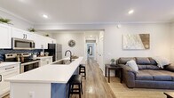 Located on Grand Ave in Palm Coast, Florida, this thoughtfully designed single-story home offers four bedrooms and three bathrooms within a well-utilized floor plan. The open-concept kitchen and living area serves as the heart of the home, featuring white shaker cabinetry, a bold navy herringbone tile backsplash, stainless steel appliances, and a striking blue-accented island with a built-in sink and bar seating — ideal for casual dining and entertaining. The living room flows seamlessly from the kitchen, highlighted by crown molding, recessed lighting, and warm hardwood-style flooring that runs throughout the home. Natural light enters through multiple windows, lending a bright and airy feel to the space. The primary bedroom provides a comfortable retreat with dual windows dressed in neutral curtains, hardwood-style floors, and direct access to one of the three bathrooms. Additional bedrooms are well-proportioned and share a consistent design palette of soft gray walls and warm flooring. The bathrooms are finished with white shaker vanities, matte black hardware, and wood-framed mirrors, adding a modern yet warm character. Every detail reflects a clean, contemporary aesthetic suited for comfortable everyday living in Palm Coast.