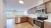 Located at 10 Townsend Lane in Brunswick, Maine, this 2-bedroom, 2-bathroom single-floor residence offers a functional and well-appointed layout. The open-plan kitchen and living area serves as the heart of the home, featuring light hardwood-style flooring throughout. The kitchen is equipped with rich walnut-toned cabinetry, white countertops, a classic subway tile backsplash, and a full suite of stainless steel appliances including a refrigerator, electric range, built-in microwave, and dishwasher. The living area provides ample room and is bathed in natural light from multiple windows, complemented by a wall-mounted mini-split HVAC unit and baseboard heating. Both bedrooms are carpeted and painted in soft blue-gray tones, each featuring a window with exterior views and baseboard heating. The primary bedroom includes access to a closet. The two bathrooms are finished with light hardwood-style flooring, wood-toned vanity cabinetry, and white countertops; one bathroom includes a tub/shower combination. The overall design is clean and contemporary, with a neutral palette that creates a bright, cohesive living environment throughout.