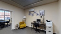 Located at 626 Lehman St in Columbus, Ohio, this single-floor professional office suite offers a well-organized and thoughtfully designed workspace suited for a variety of business needs. The suite comprises several distinct functional areas that work together to create a cohesive and productive environment.

The private office is a focused, efficiently arranged workspace featuring a dark wood industrial-style desk, an ergonomic task chair, a desktop computer, and a dedicated printer/copier unit. A striking yellow accent armchair with a stylish floor lamp adds a welcoming touch, while a wall-mounted mini-split system ensures individualized climate control. A gallery of black-and-white framed photographs of Columbus landmarks lends a sense of local character throughout the space.

The conference room seats multiple occupants around a substantial dark wood table and is equipped with a wall-mounted flat-screen display, making it ideal for presentations and collaborative meetings. A large window brings in natural light and provides views of the surrounding neighborhood, while a wall-mounted mini-split and decorative greenery enhance the room's comfort and ambiance.

A shared open workstation area accommodates two desks with computers and is brightened by recessed panel lighting, offering a bright and efficient environment for collaborative or support staff work.

The reception and transitional lounge area connects the spaces gracefully, featuring the signature yellow armchair, warm accent lighting, and framed artwork — creating an inviting first impression for clients and visitors alike. Neutral carpet flooring and a soft, neutral color palette unify the entire suite.