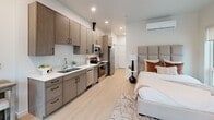 This 360 square foot studio apartment in Salt Lake City showcases a modern and efficient design. The open-concept layout maximizes space utilization, seamlessly integrating living, sleeping, and dining areas. The kitchen features sleek cabinetry, stainless steel appliances, and a functional workspace. The sleeping area includes a comfortable bed and a small seating arrangement near large windows, allowing natural light to fill the space. A stylish bathroom with a vanity, toilet, and shower completes the unit. Light wood flooring throughout creates a cohesive look, while the neutral color palette enhances the sense of spaciousness. Thoughtful touches like recessed lighting, wall-mounted air conditioning, and carefully chosen artwork contribute to the apartment's contemporary ambiance. Despite its compact size, the studio offers ample storage solutions and a well-planned layout, making it an ideal urban living space.